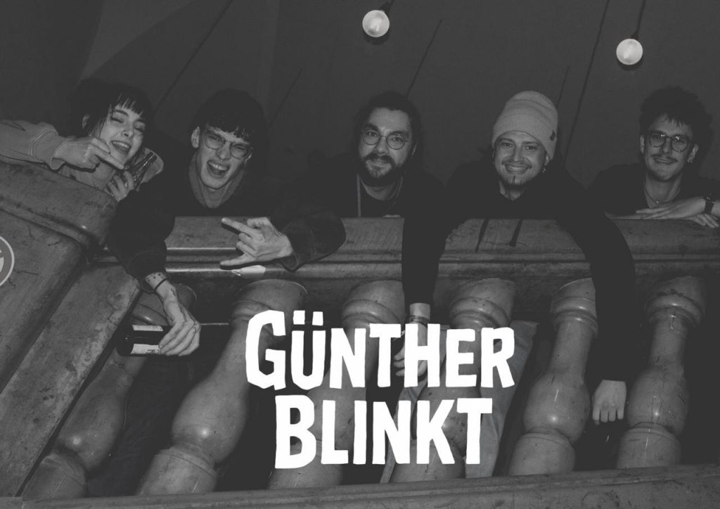 Das Bild zeigt die fünf Mitglieder der Punkrock-Band Günther Blinkt, die sich über ein massives Geländer lehnen. Darunter ist der Bandname eingeblendet.