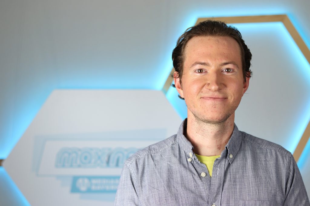 Das Foto zeigt den Praktikanten Simun-Petar Krizanac vor dem max neo Logo.