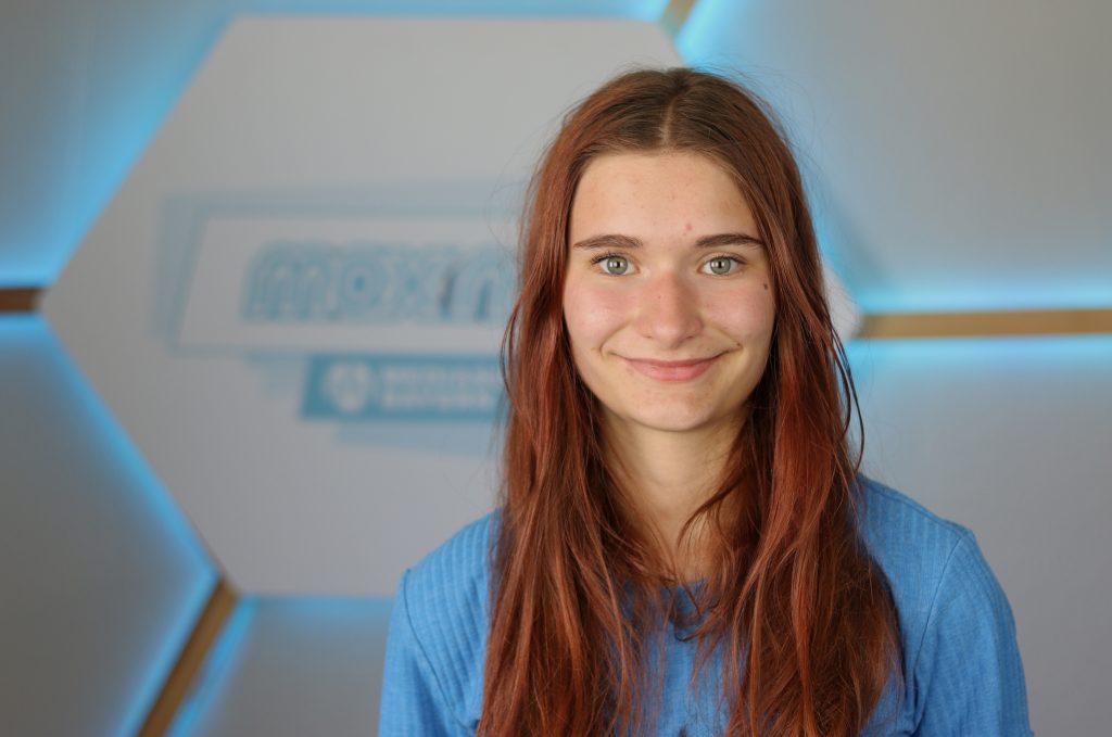 das Foto zeigt die Praktikantin Paula Zapf im Porträt vor dem max neo Logo.